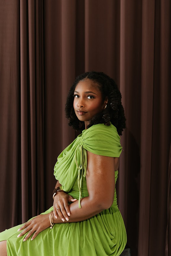 Kierra Dotson seated in a green dress against a draped curtain backdrop